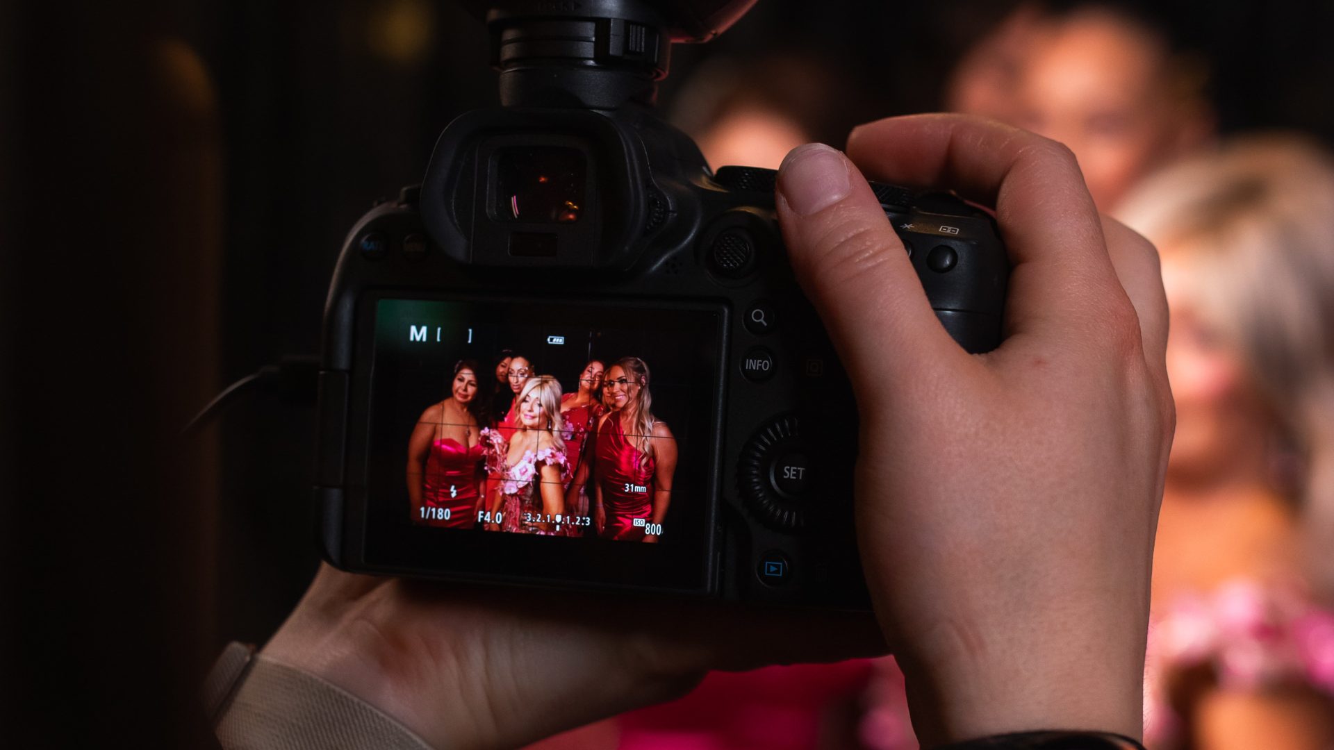 Photographer capturing group of women in red dresses using DSLR camera, with smartphone preview, at an event.