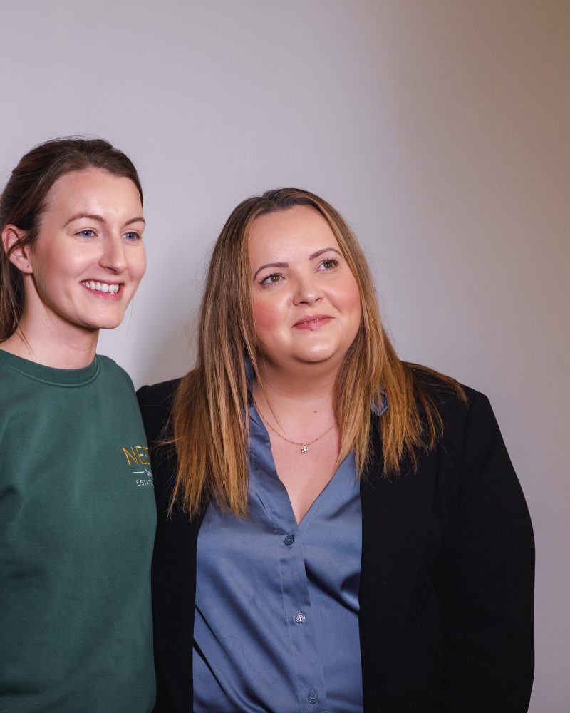 Two women smiling for a photo in casual and business attire at an event.