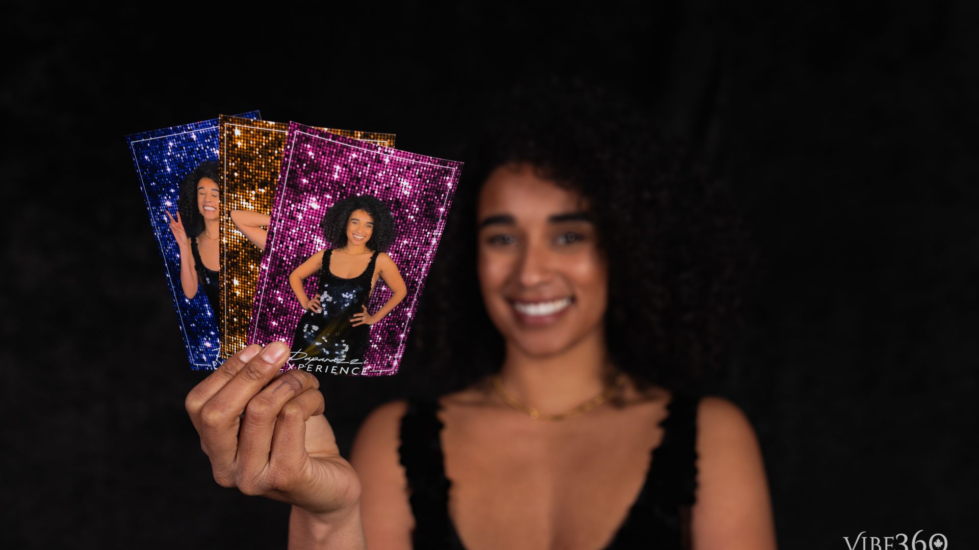 Woman holding colorful photo cards with smiling portraits against a dark background.
