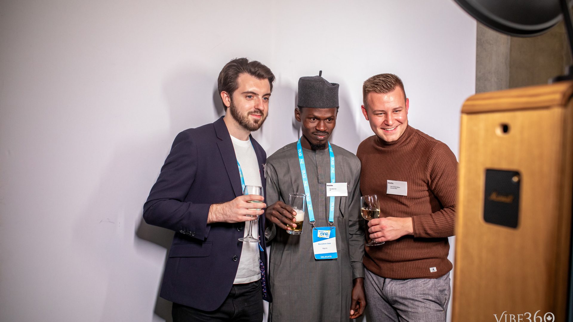 Three men posing with drinks at a networking event photo booth, smiling and looking at the camera.