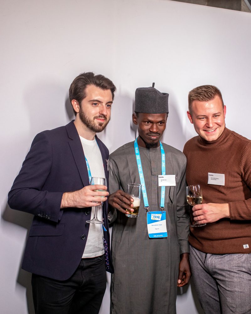 Three men posing with drinks at a networking event photo booth, smiling and looking at the camera.