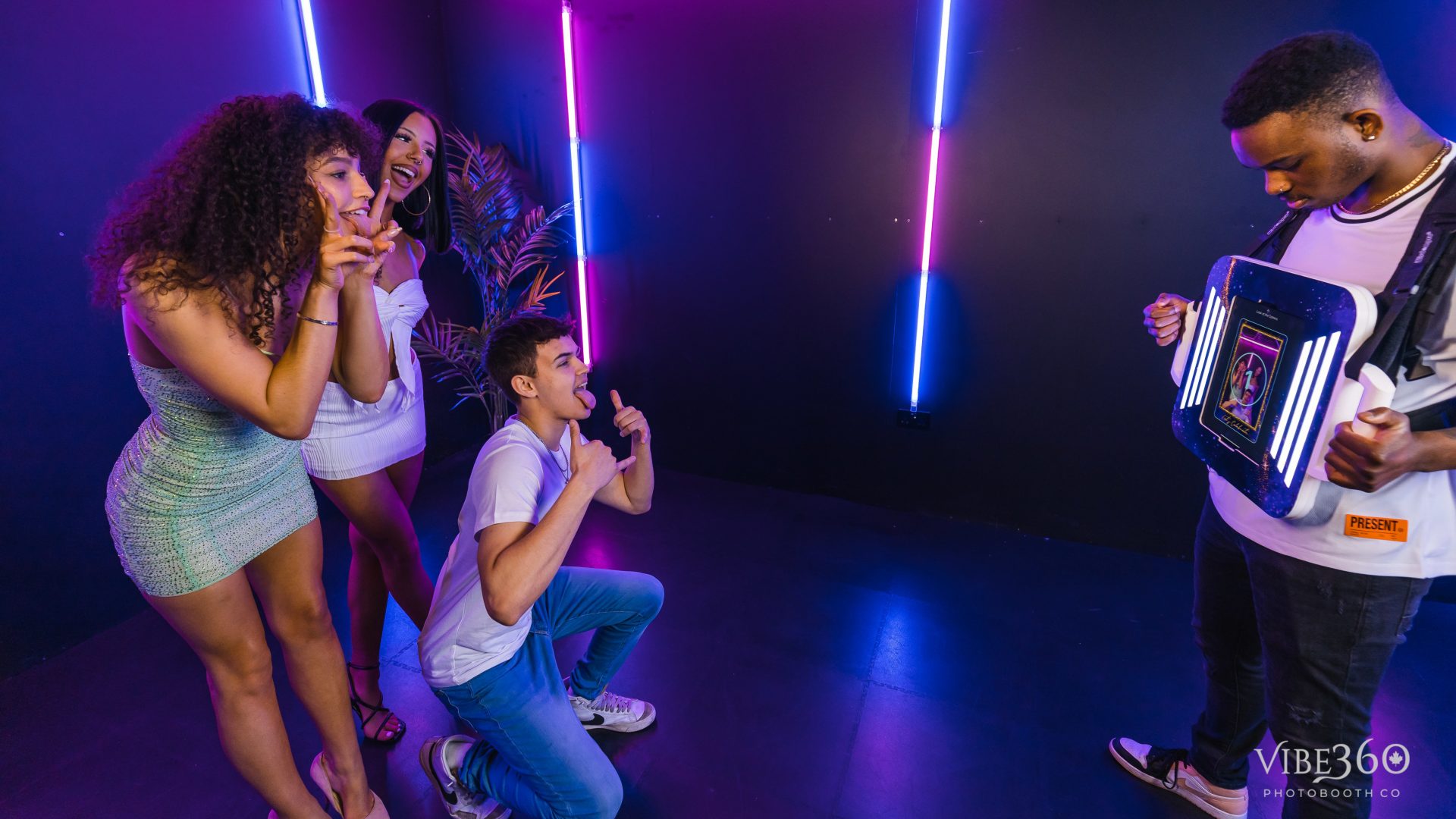 Group of friends posing with neon lights and a futuristic device in a fun, vibrant atmosphere.