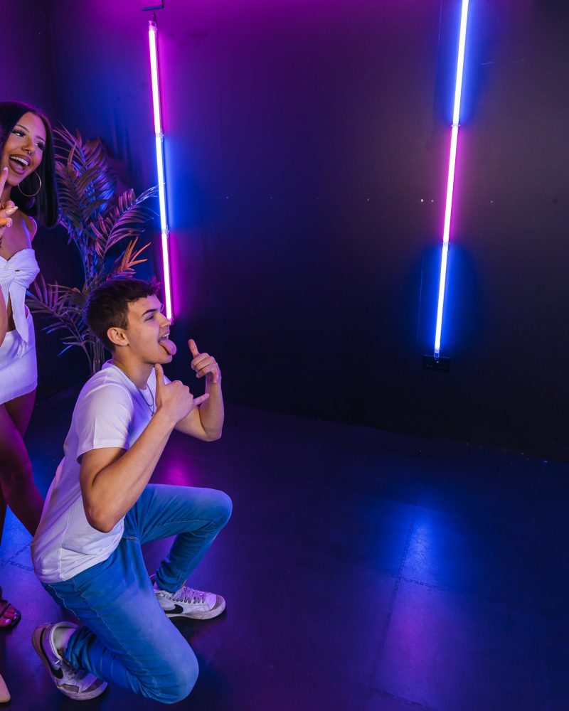 Group of friends posing with neon lights and a futuristic device in a fun, vibrant atmosphere.