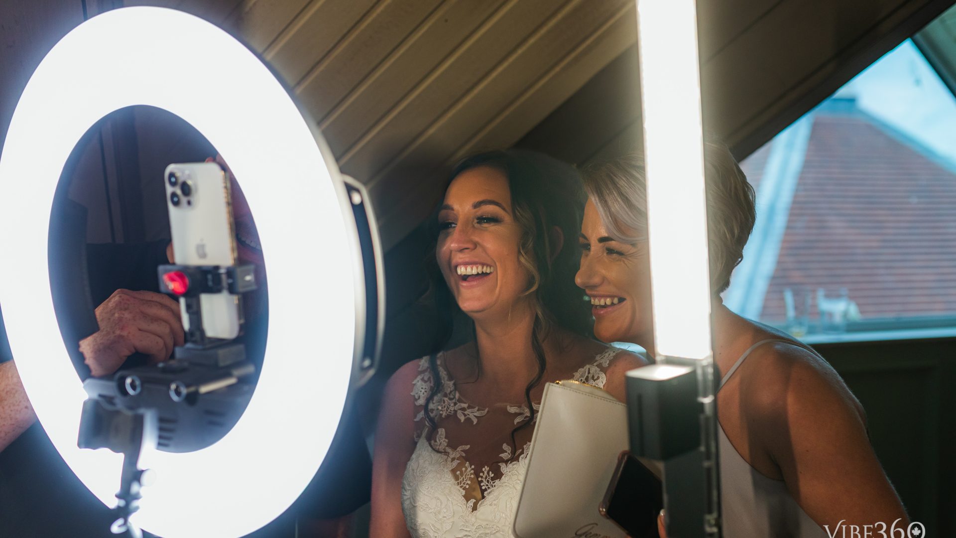 Two women enjoying a lighted photobooth experience with a ring light and smartphone, captured at a joyful event.