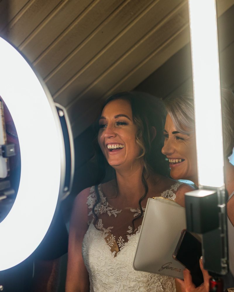 Two women enjoying a lighted photobooth experience with a ring light and smartphone, captured at a joyful event.