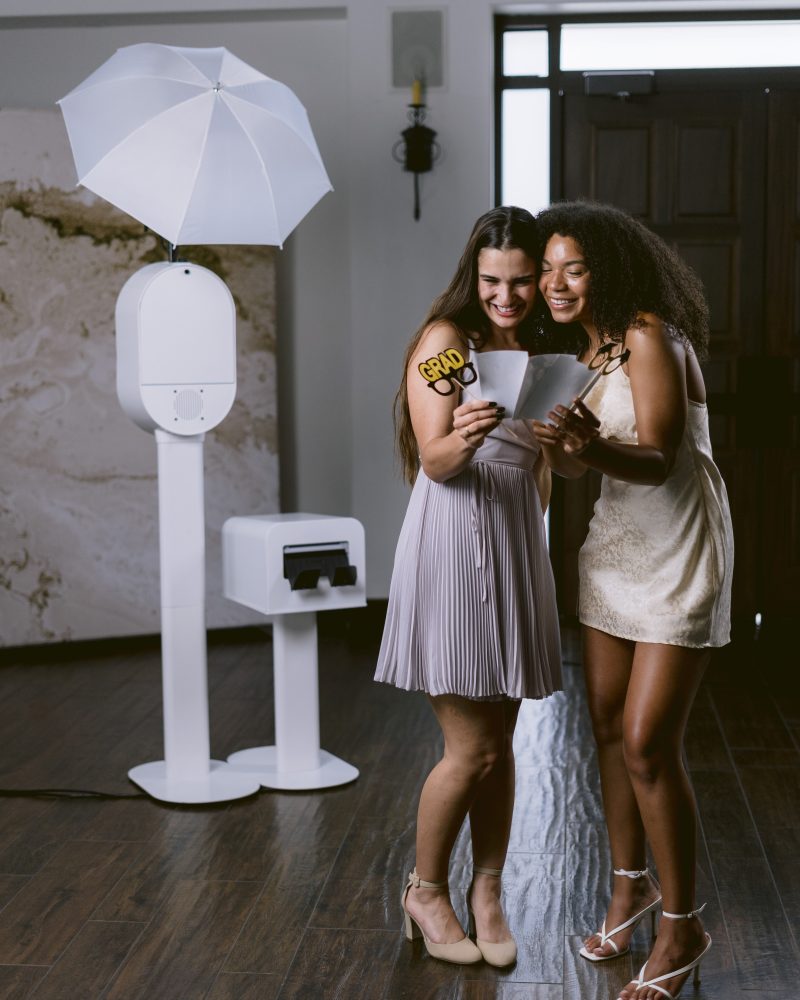 Two friends celebrating graduation with a photo booth session, holding Grad props and smiling.