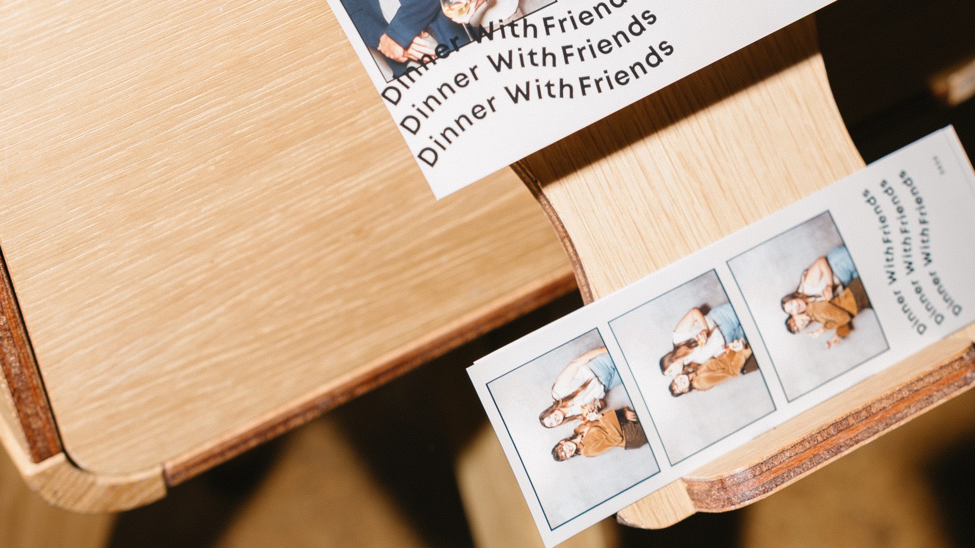 Photo booth prints labeled Dinner With Friends sliding from a wooden dispenser, showcasing candid moments.