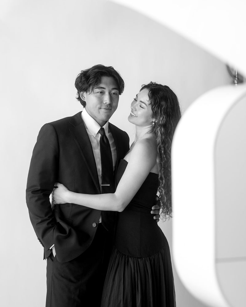 Elegant couple embraces in formal attire during a black-and-white photography session.