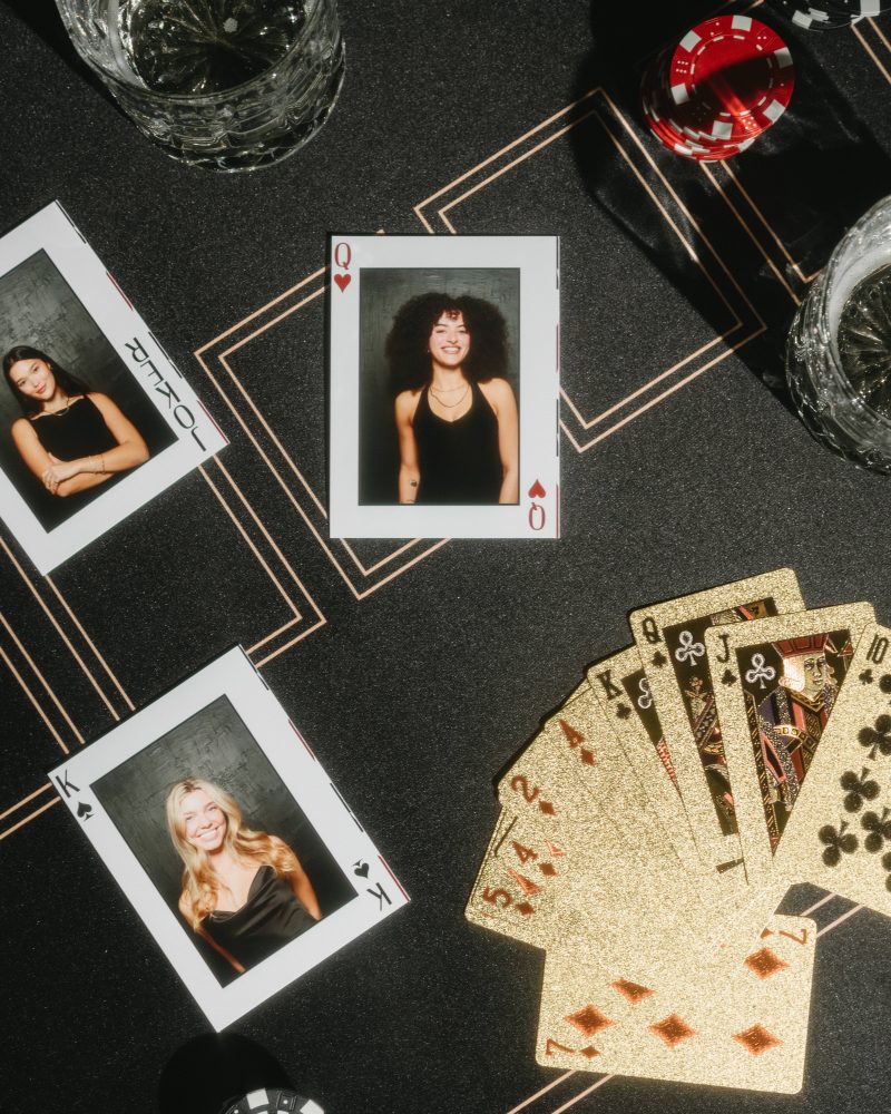 Poker-themed flat lay with playing cards, personal photos, poker chips, and drinks on a dark surface.