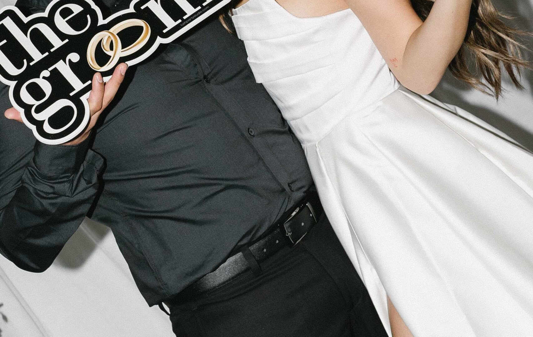 Bride and groom smiling at each other, holding playful wedding signs.