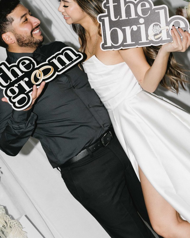 Bride and groom smiling at each other, holding playful wedding signs.