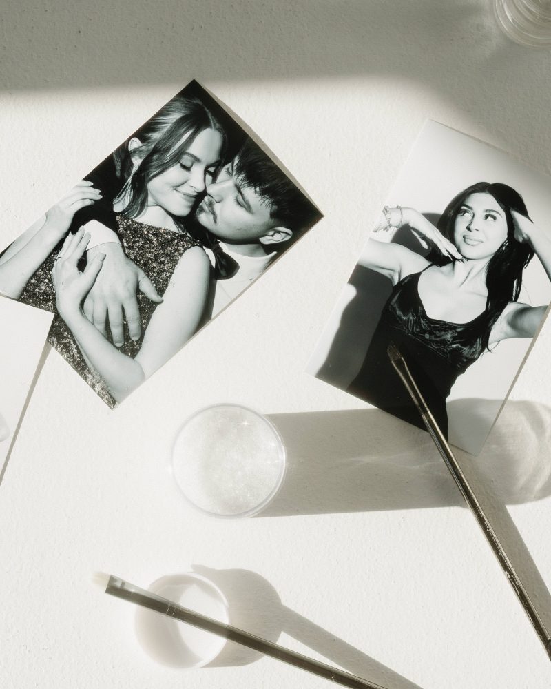 Three black and white photos on a sunlit table with cosmetic tools and jars, capturing elegant poses and intimate moments.