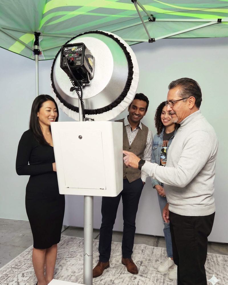 Group of four people using a modern photo booth under a green canopy tent.