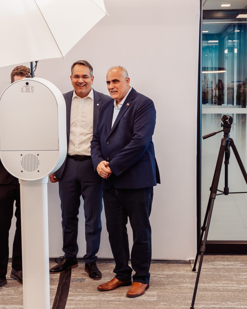 Two men posing in a modern office setting with a photo booth and tripod camera.