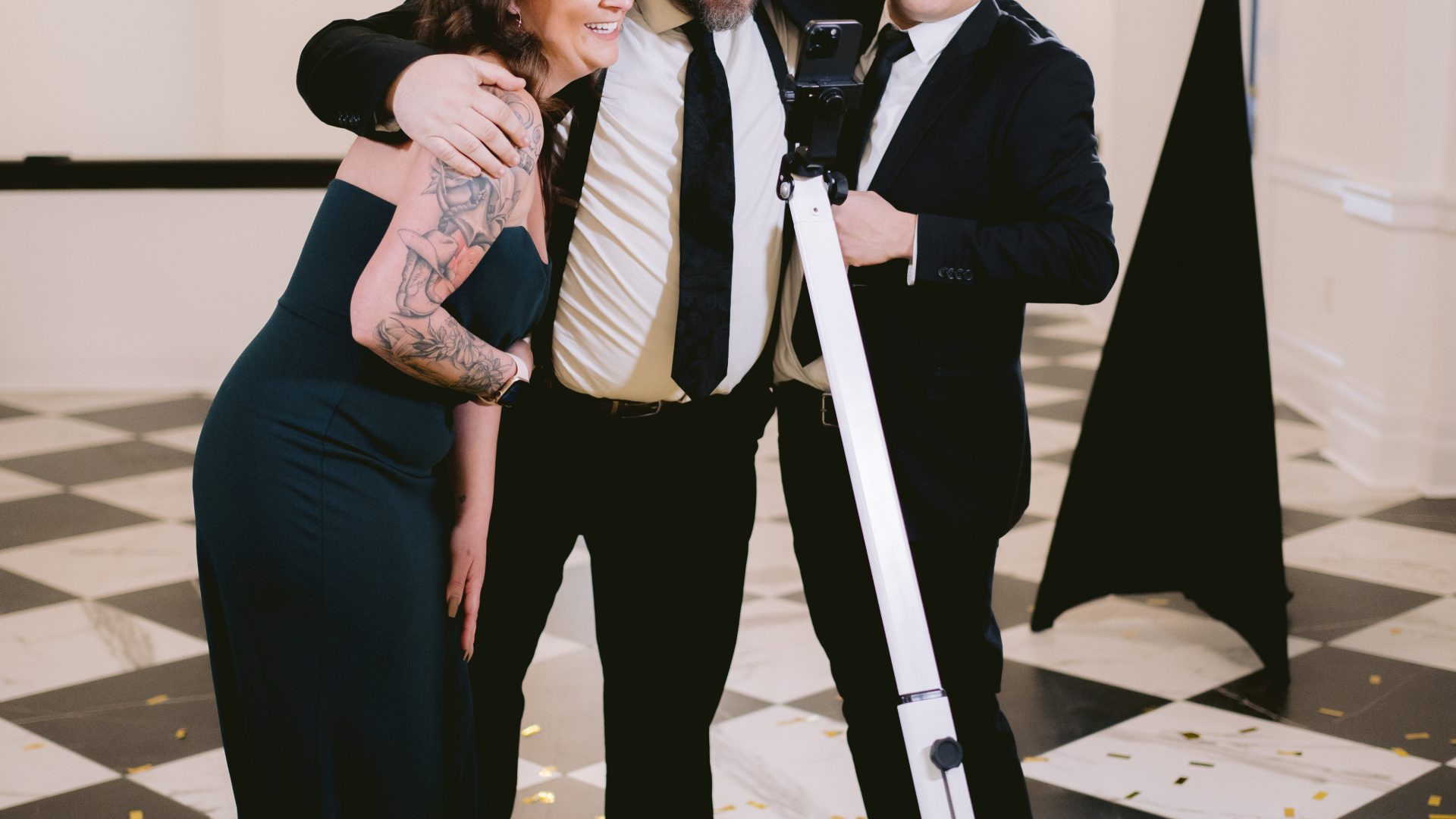 Three people celebrating at a photobooth event with gold confetti on a checkered floor.